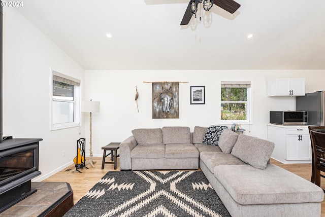 living room featuring light hardwood / wood-style floors, a wood stove, ceiling fan, and lofted ceiling