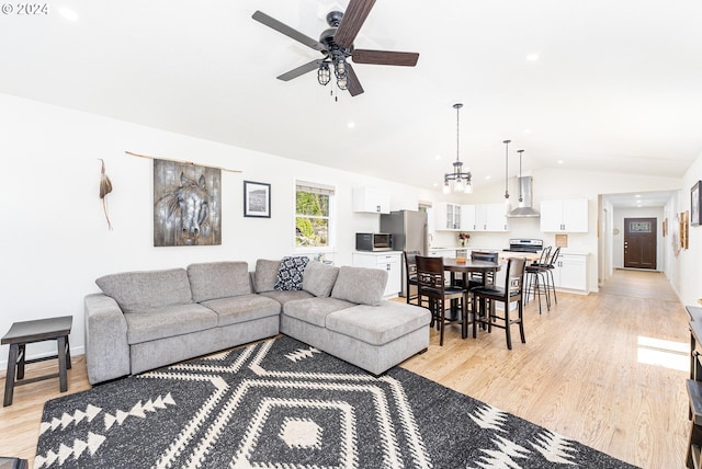 living area with lofted ceiling, light wood-style flooring, baseboards, and ceiling fan with notable chandelier