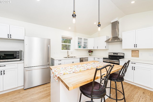 kitchen with appliances with stainless steel finishes, glass insert cabinets, wall chimney range hood, and white cabinetry