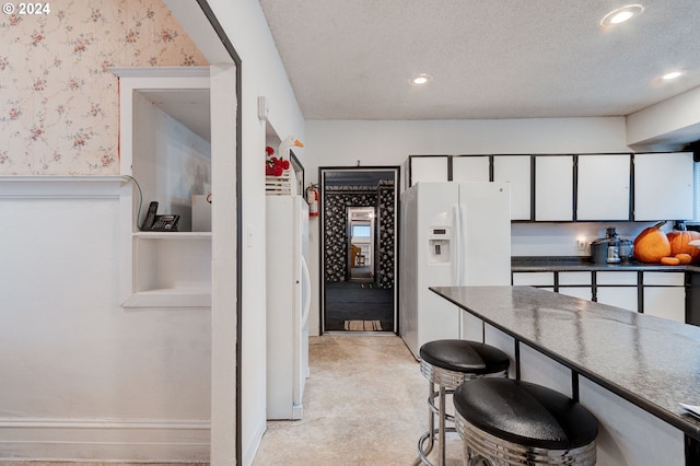 kitchen with white cabinets, white fridge with ice dispenser, and a textured ceiling