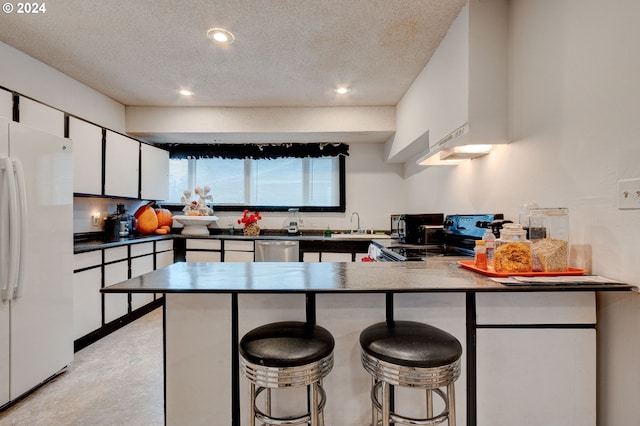 kitchen with a kitchen breakfast bar, stainless steel dishwasher, a textured ceiling, white fridge, and white cabinetry