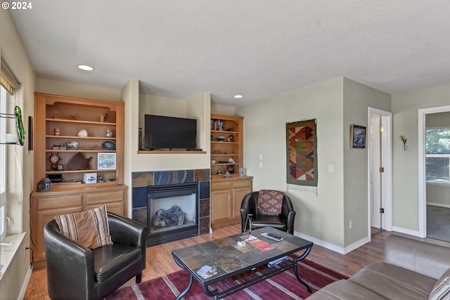 living room featuring a tiled fireplace, wood-type flooring, and a textured ceiling