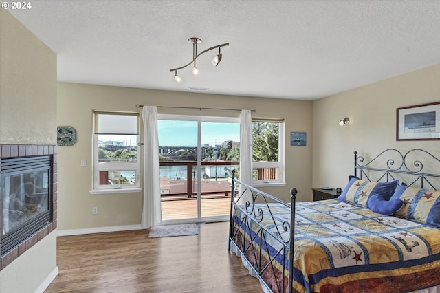 bedroom with wood-type flooring, access to outside, multiple windows, and a tiled fireplace