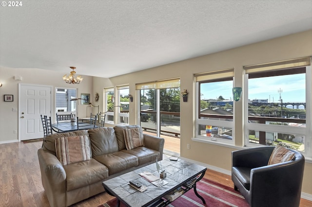 living room with hardwood / wood-style floors, a water view, a textured ceiling, and an inviting chandelier