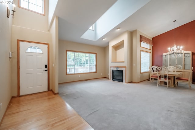 interior space featuring light hardwood / wood-style flooring, a tile fireplace, a chandelier, high vaulted ceiling, and a skylight