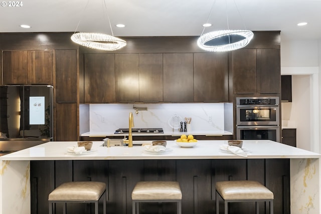 kitchen featuring decorative light fixtures, a kitchen bar, stainless steel double oven, and a kitchen island with sink