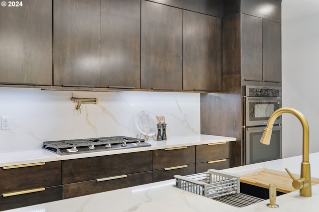 kitchen featuring dark brown cabinetry, decorative backsplash, light stone countertops, and stainless steel gas stovetop