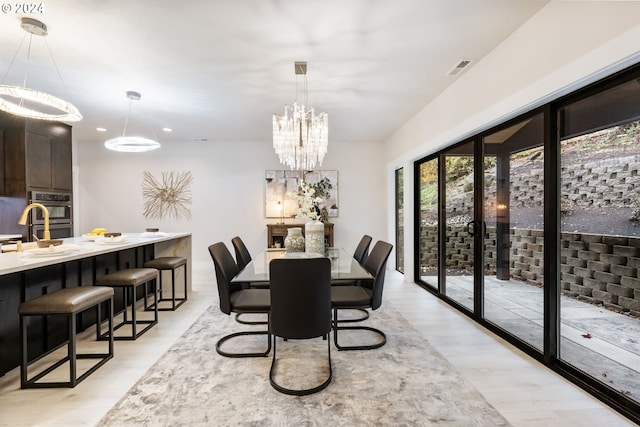 dining space with sink, an inviting chandelier, and light wood-type flooring