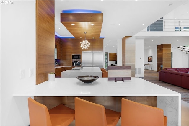 kitchen featuring an island with sink, built in appliances, a kitchen breakfast bar, hanging light fixtures, and an inviting chandelier