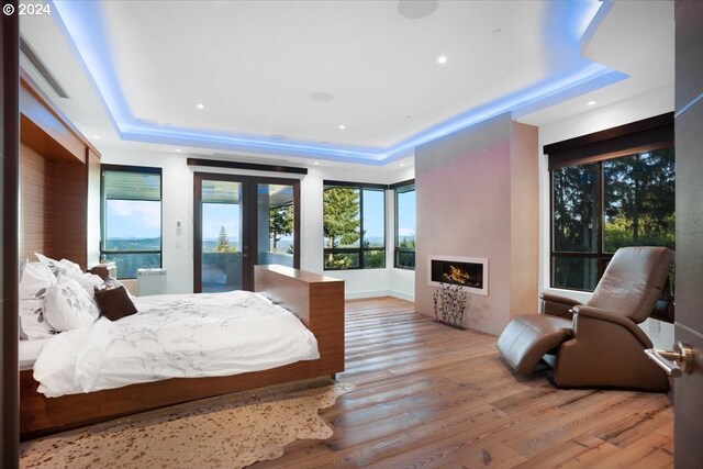 bedroom featuring access to exterior, a tray ceiling, light wood-type flooring, and a fireplace