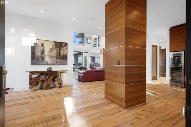 corridor with beverage cooler, light wood-type flooring, and a high ceiling