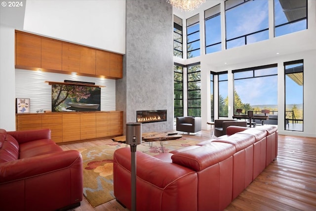 living room with light hardwood / wood-style flooring, a chandelier, a large fireplace, and a high ceiling