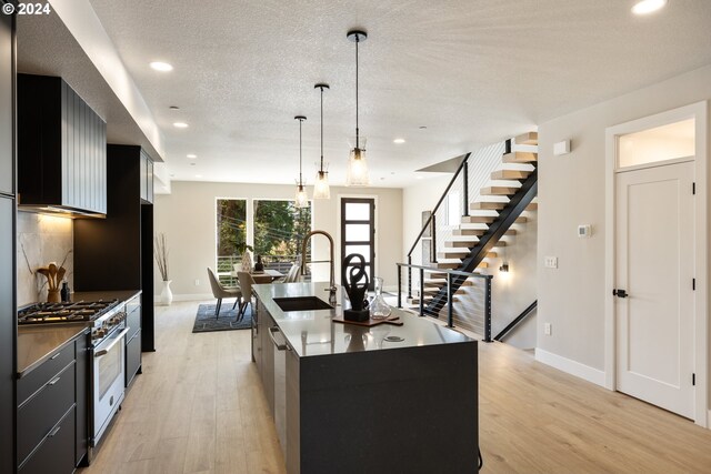 kitchen with range with gas cooktop, sink, light hardwood / wood-style floors, hanging light fixtures, and a kitchen island with sink