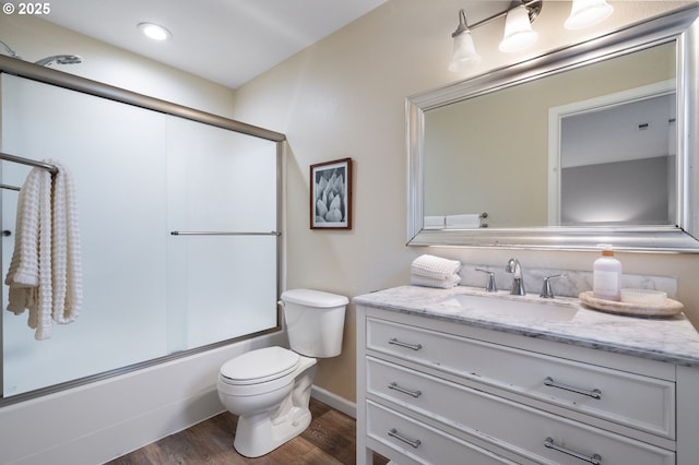 full bathroom featuring toilet, vanity, wood-type flooring, and combined bath / shower with glass door