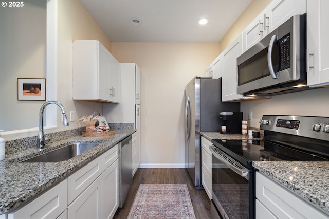 kitchen with appliances with stainless steel finishes, light stone counters, dark wood-type flooring, sink, and white cabinetry