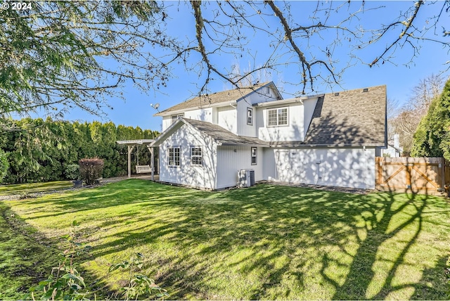 rear view of house with a yard, cooling unit, roof with shingles, and fence