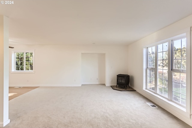 carpeted spare room featuring visible vents, a wood stove, and baseboards