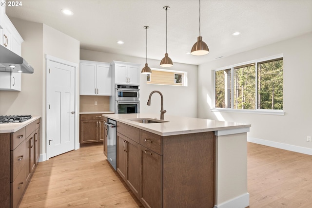 kitchen featuring sink, light hardwood / wood-style flooring, a kitchen island with sink, decorative light fixtures, and white cabinetry