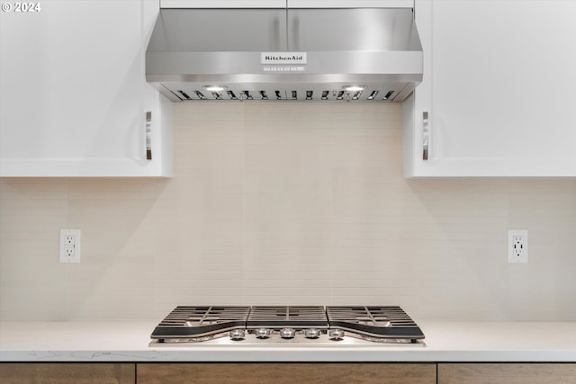 kitchen with stainless steel gas stovetop, white cabinetry, light stone countertops, and wall chimney range hood