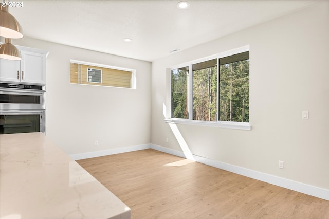 kitchen with light stone countertops, light wood-type flooring, white cabinetry, and stainless steel double oven