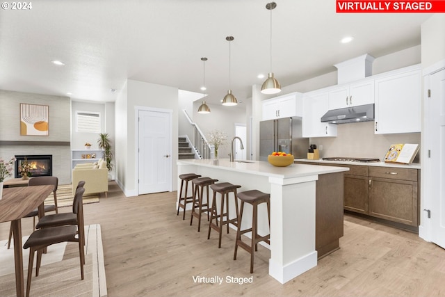 kitchen featuring light wood-type flooring, stainless steel appliances, a center island with sink, decorative light fixtures, and a large fireplace