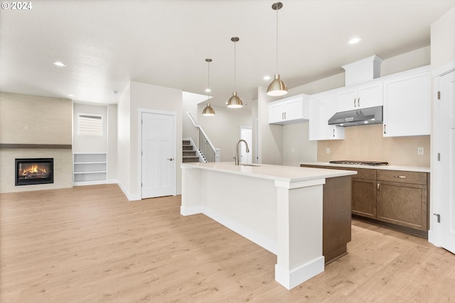 kitchen featuring sink, a kitchen island with sink, white cabinetry, a fireplace, and light wood-type flooring