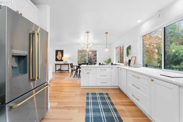 kitchen featuring white cabinetry, high end fridge, decorative light fixtures, and light wood-type flooring