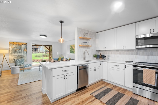 kitchen with stainless steel appliances, decorative light fixtures, sink, white cabinets, and light hardwood / wood-style flooring