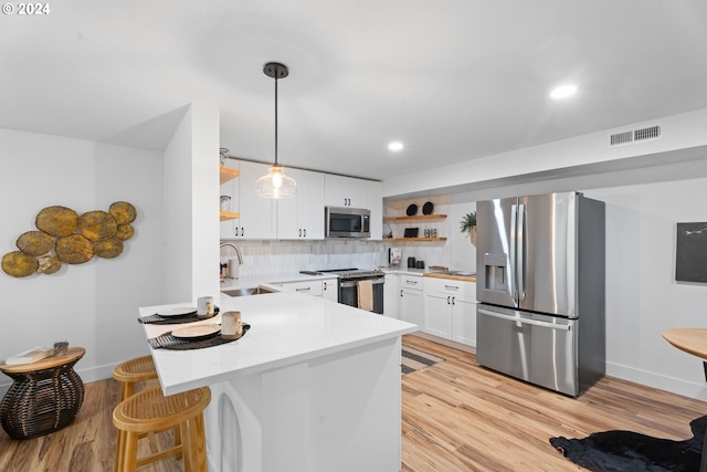 kitchen featuring white cabinetry, sink, kitchen peninsula, appliances with stainless steel finishes, and decorative light fixtures