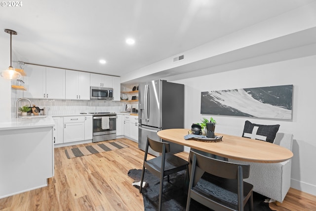 kitchen with white cabinetry, sink, appliances with stainless steel finishes, hanging light fixtures, and light hardwood / wood-style flooring