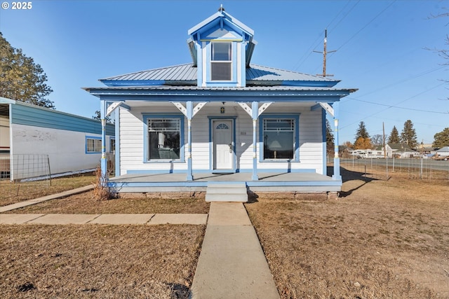 view of front of property featuring covered porch, fence, metal roof, and a front yard