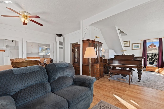 living room with light wood-style floors, a ceiling fan, and a textured ceiling