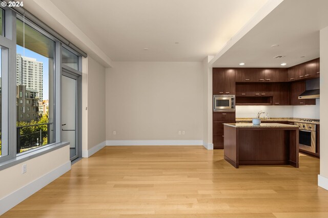 kitchen featuring dark brown cabinets, light hardwood / wood-style floors, a kitchen island with sink, wall chimney range hood, and stainless steel appliances