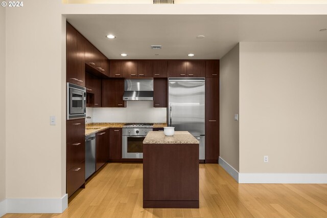 kitchen with built in appliances, light hardwood / wood-style flooring, extractor fan, and a kitchen island