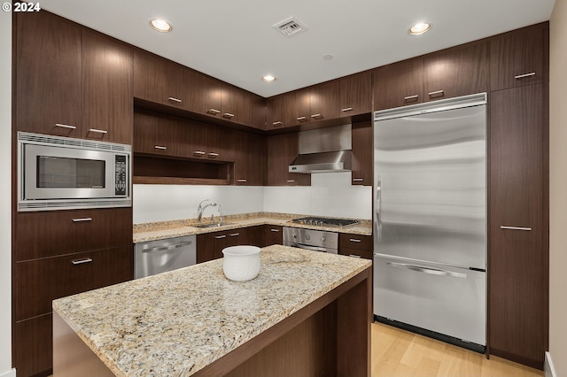 kitchen featuring light hardwood / wood-style floors, built in appliances, range hood, and light stone counters