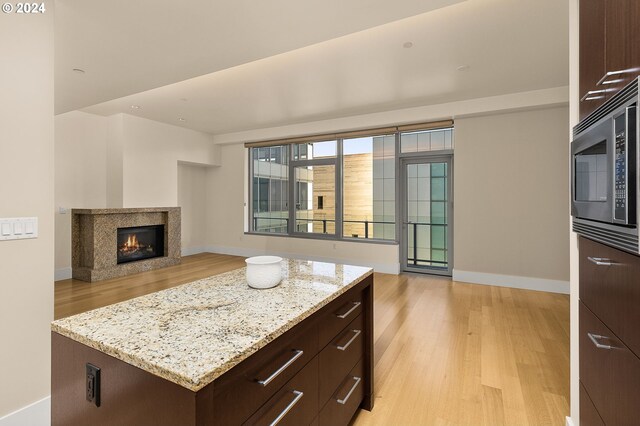 kitchen featuring stainless steel microwave, light stone countertops, dark brown cabinets, a center island, and light hardwood / wood-style flooring