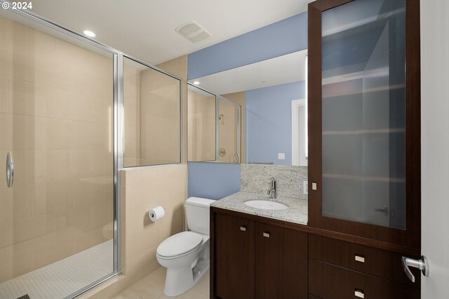 bathroom with vanity, tile patterned floors, tile walls, toilet, and a shower with door