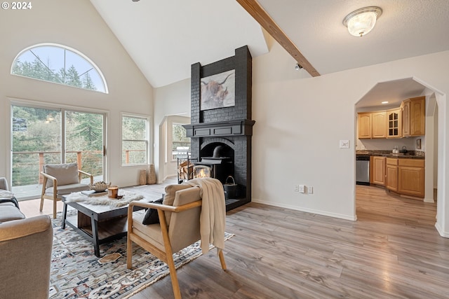 living room with beamed ceiling, a wood stove, light hardwood / wood-style floors, and high vaulted ceiling