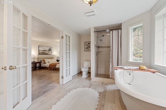 bathroom with toilet, hardwood / wood-style floors, separate shower and tub, and french doors