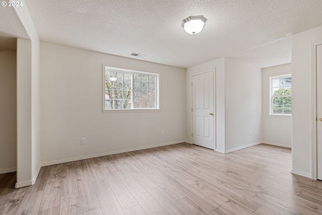 unfurnished bedroom featuring a textured ceiling, light hardwood / wood-style flooring, and multiple windows