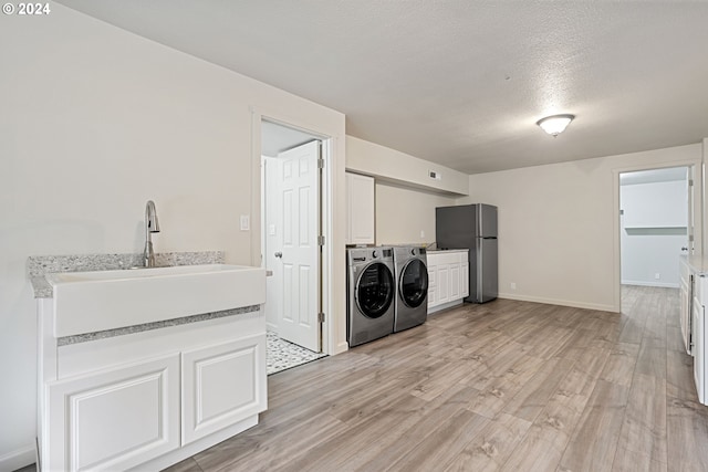 laundry room featuring sink, cabinets, separate washer and dryer, light hardwood / wood-style flooring, and a textured ceiling