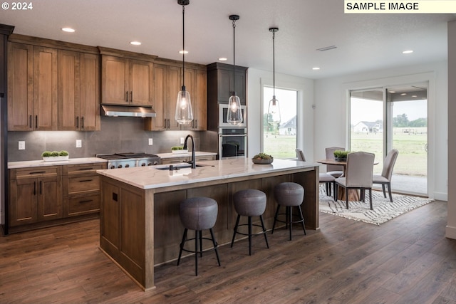 kitchen with sink, decorative light fixtures, backsplash, a kitchen island with sink, and dark wood-type flooring