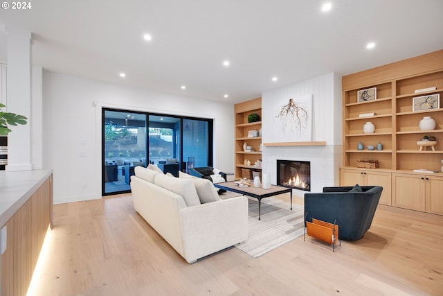 living room with light hardwood / wood-style floors, built in shelves, and a tile fireplace