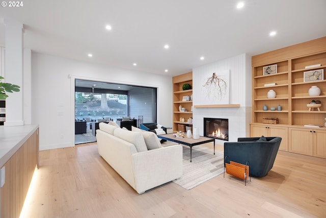 living room featuring light wood-type flooring, built in shelves, and a fireplace