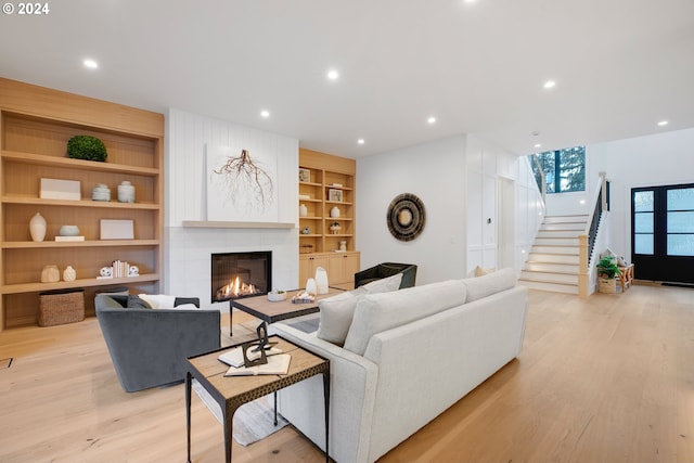 living room with light wood-type flooring, built in shelves, and a fireplace