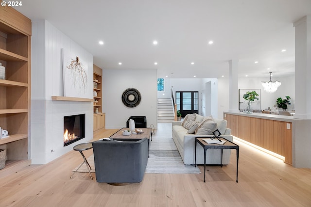 living room with light wood-type flooring, a large fireplace, a chandelier, and built in shelves