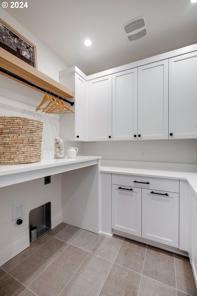 laundry area with electric dryer hookup, light tile patterned floors, and cabinets