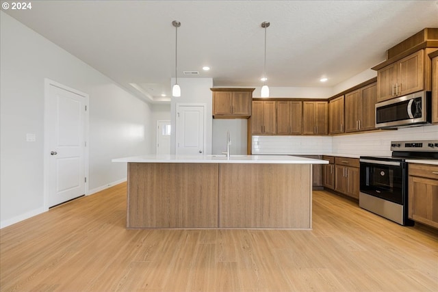 kitchen featuring a center island with sink, pendant lighting, stainless steel appliances, and light hardwood / wood-style floors