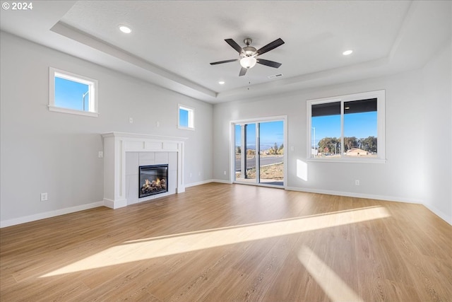 unfurnished living room featuring ceiling fan, a raised ceiling, light wood-type flooring, and a tile fireplace