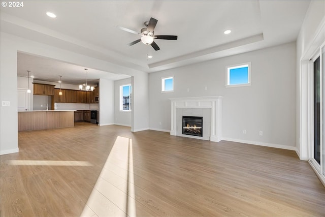 unfurnished living room featuring light hardwood / wood-style flooring, a tile fireplace, and ceiling fan with notable chandelier